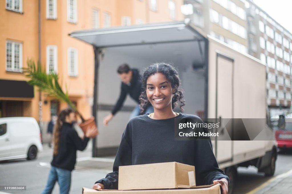 Portrait of confident female mover carrying boxes