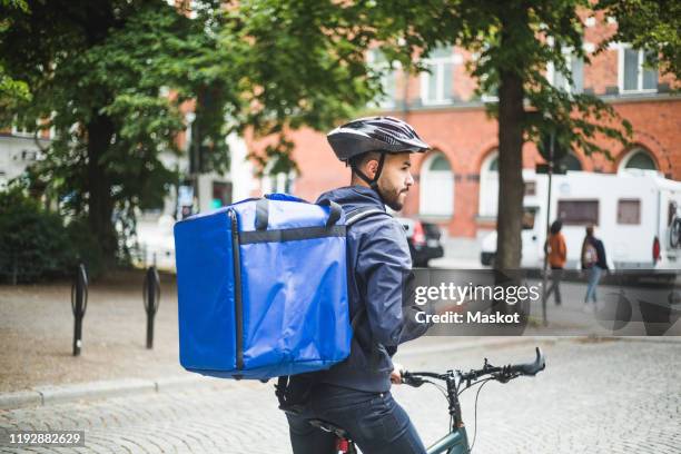 food delivery man with bicycle looking away while standing on street in city - bike messenger stock pictures, royalty-free photos & images