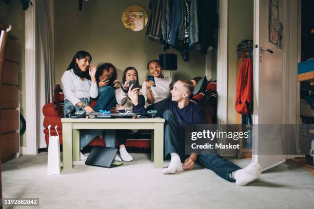 cheerful friends talking while looking at smart phone in living room - five people stock pictures, royalty-free photos & images