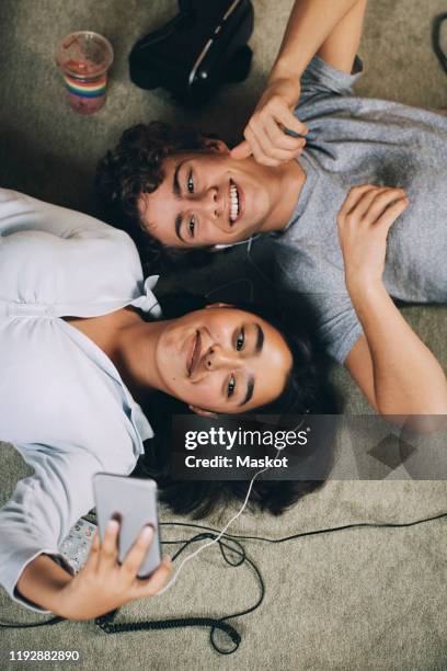 directly above shot of teenage girl taking selfie with friend while lying together on carpet at home - grupo de adolescentes imagens e fotografias de stock