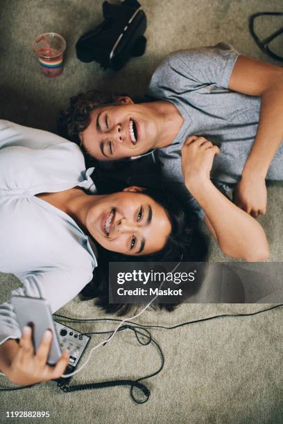 directly above shot of happy friends listening music together while lying on carpet at home - lying down friends girls stock pictures, royalty-free photos & images