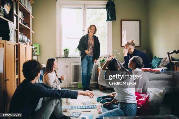 friends looking at teenage boy talking while playing board games at home - game night leisure activity stock pictures, royalty-free photos & images