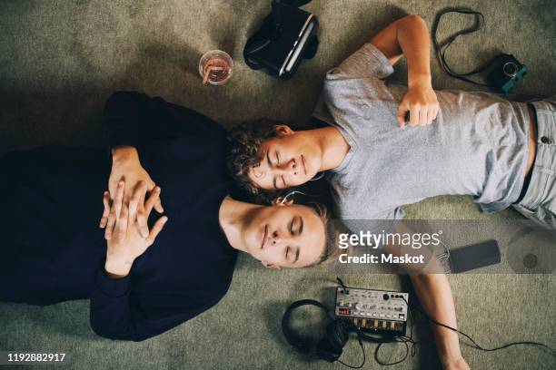 directly above shot of male teenagers with closed eyes listening music while lying on carpet at home - liebe teilen stock-fotos und bilder