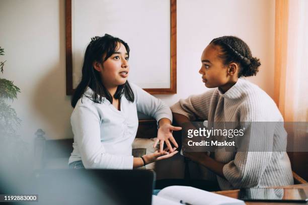 teenage girl gesturing while talking to friend on sofa in living room - friends talking living room stock-fotos und bilder