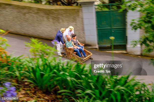 tourists taking a ride in a tradional wicker toboggan down the hill from monte in funchal on madeira island in portugal - wicker stock pictures, royalty-free photos & images