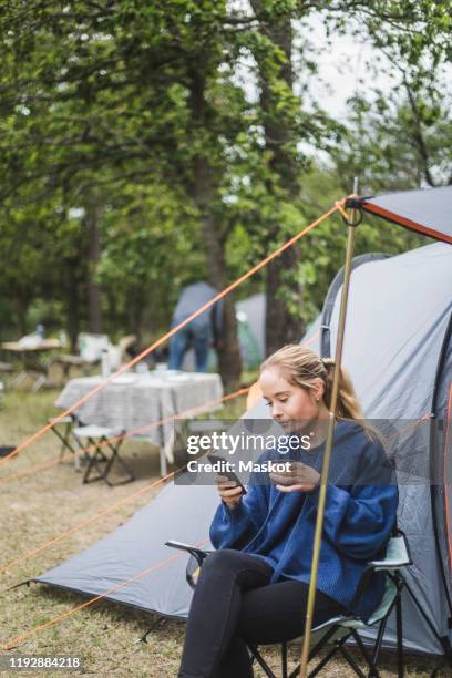 teenage girl using mobile phone while having coffee against tent - camping chair stock pictures, royalty-free photos & images