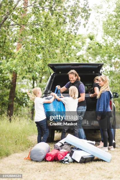 children assisting parents in unloading luggage from car trunk at camping site - car camping luggage imagens e fotografias de stock