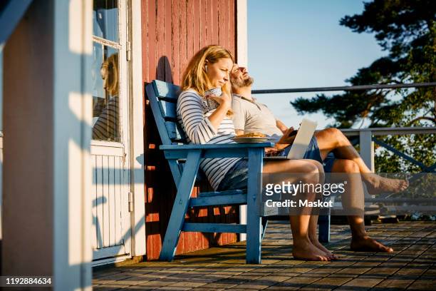 mid adult woman using laptop while having breakfast and sitting with man at porch - sitting outside stock pictures, royalty-free photos & images