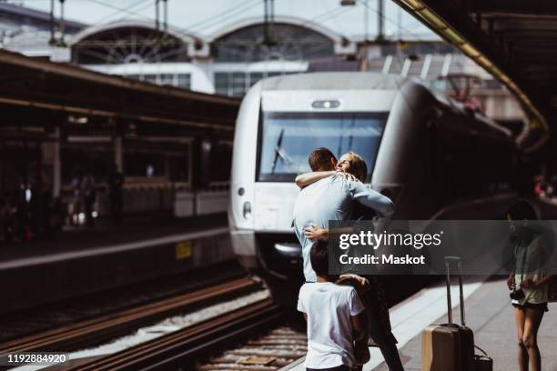 children looking at parents embracing on railroad station platform - quai de gare photos et images de collection