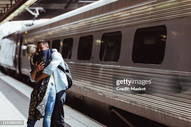 loving couple embracing by train on railroad station platform at station - arrivée photos et images de collection