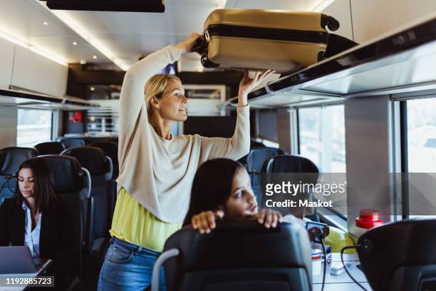 woman arranging luggage on shelf while traveling with children in train - luggage stockfoto's en -beelden