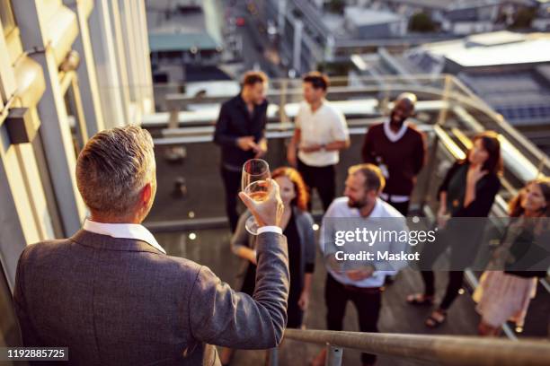 mature businessman raising toast while giving speech to colleagues in terrace - kick off stock-fotos und bilder