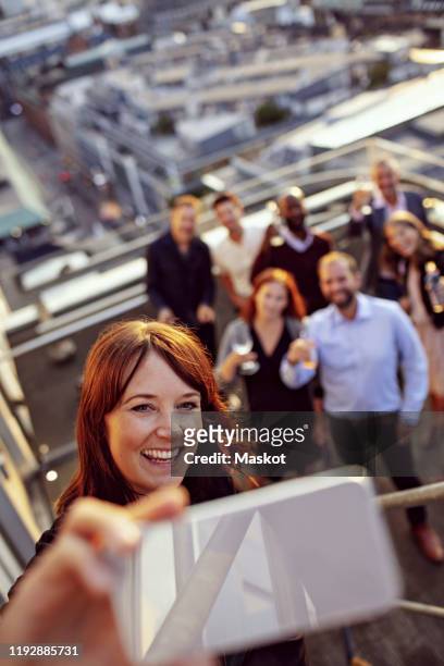 smiling businesswoman taking selfie with colleagues on smart phone during office party on terrace - kick off call stock pictures, royalty-free photos & images