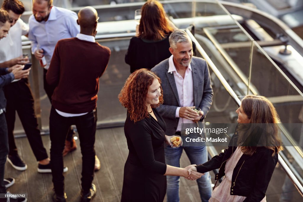 High angle view of businesswoman doing handshake and greeting while partying with coworkers after work on terrace