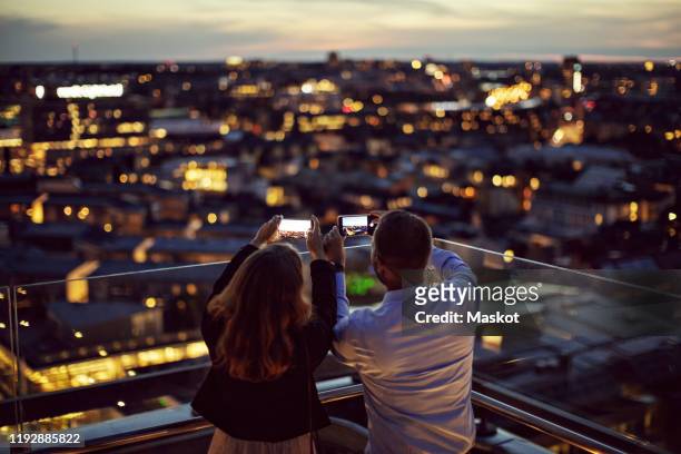 rear view of male and female professionals photographing city on mobile phone from terrace during sunset - kick off call stock pictures, royalty-free photos & images