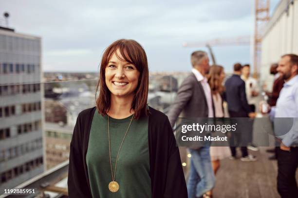 portrait of smiling businesswoman with colleagues in background standing on terrace during party - office party stock pictures, royalty-free photos & images