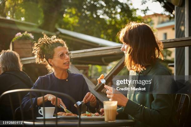 female architects discussing while having lunch at outdoor cafe during sunny day - terrasse de café photos et images de collection
