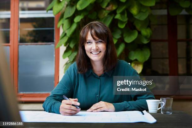 portrait of smiling female architect with blueprint at table in backyard - womens draft ストックフォトと画像