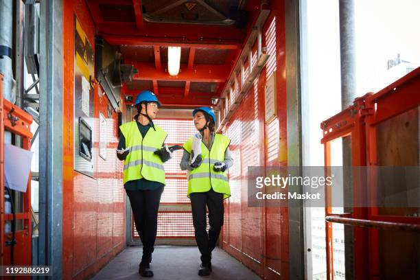 full length of female engineers discussing while walking in freight elevator at construction site - construction industry photos stock pictures, royalty-free photos & images
