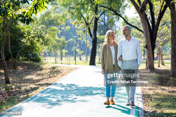 senior citizen couple taking a walking in a park during summer morning. seniors couple spend time in public park together. - lebensversicherung stock-fotos und bilder