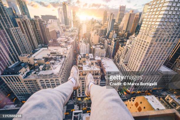 personal perspective of feet hanging down from a ledge over new york city at sunset - overhangend stockfoto's en -beelden
