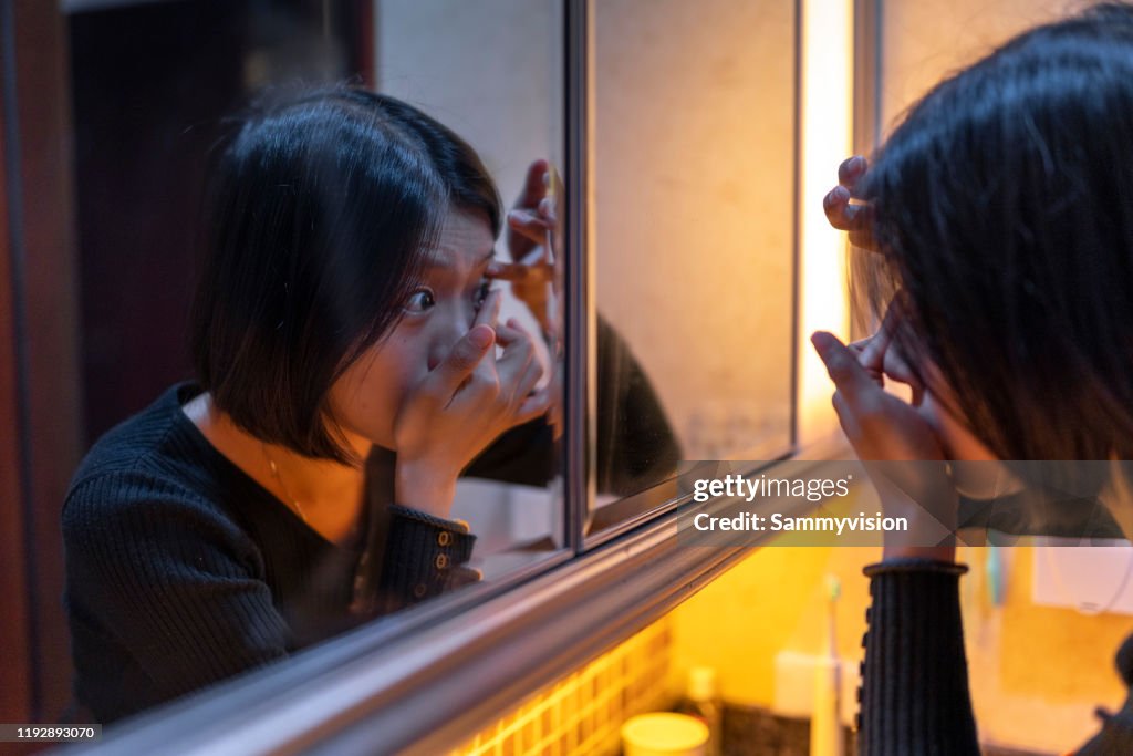 Asian woman putting contact lens in eye at home