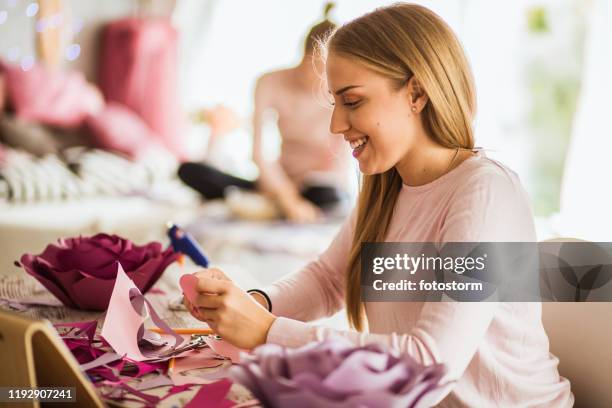 smiling young woman making paper flowers as decoration - paper flower stock pictures, royalty-free photos & images
