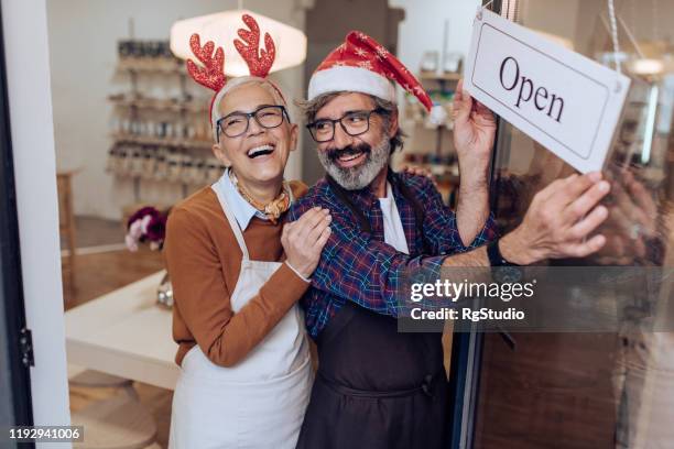 mature couple opening their shop and celebrating christmas - small business holiday shopping stock pictures, royalty-free photos & images
