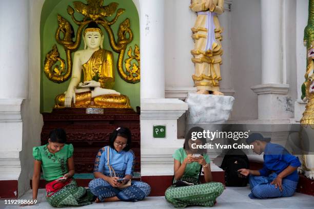 Young Burmese are absorbed by their mobile phones as they sit in front of Buddha statues and shrines at the Shwedagon pagoda in the Myanmar capital,...