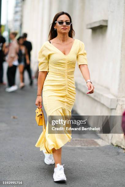 Guest wears sunglasses, a yellow seersucker v-neck, gathered and ruffled dress, a yellow bag, white sneakers, outside the Prada show during Milan...