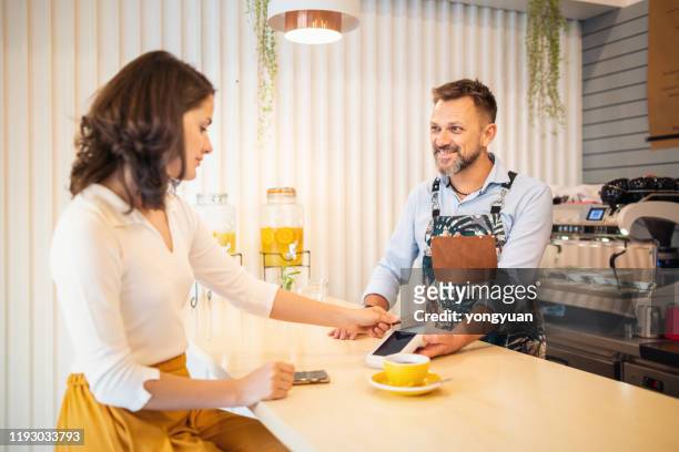 female customer tapping credit card to pay in a coffee shop - tap card stock pictures, royalty-free photos & images