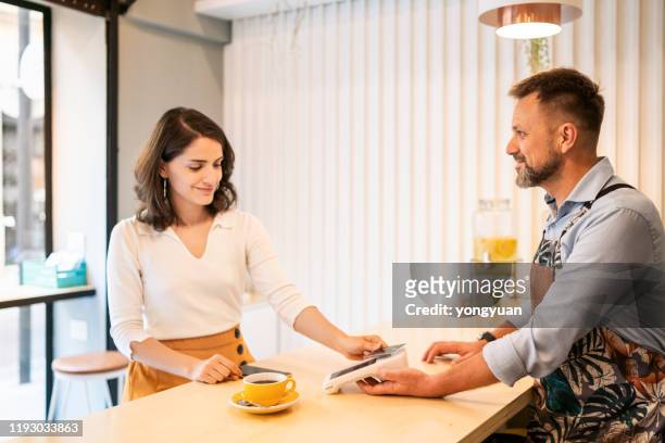 female customer tapping credit card to pay in a coffee shop - tap card stock pictures, royalty-free photos & images