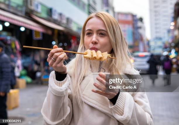 young woman eating street food at market - korean street food stock pictures, royalty-free photos & images