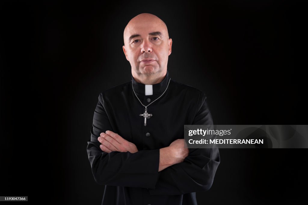 Crossed arms bald priest portrait in black background
