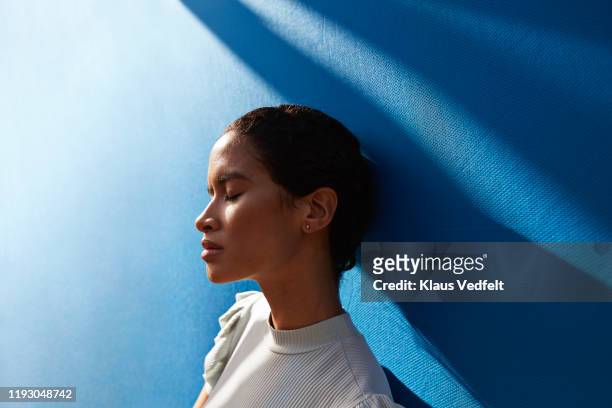beautiful woman standing against blue wall - tranquility stock-fotos und bilder