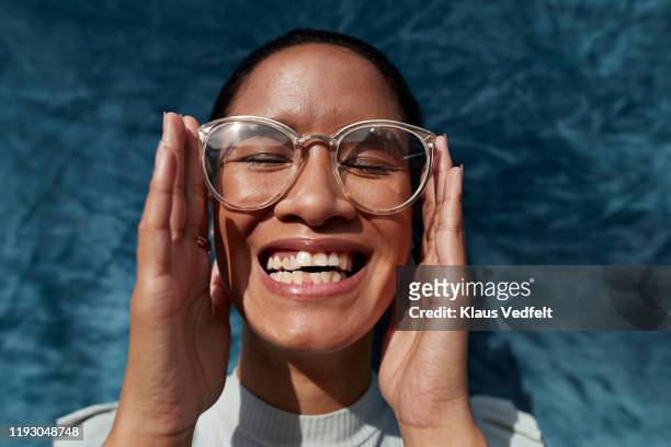 smiling woman wearing eyeglasses against blue wall - monsieur et madame tout le monde photos et images de collection