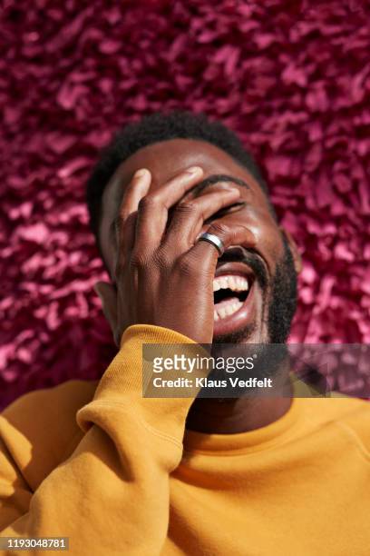 happy young man covering face against textured wall - lachen mann stock-fotos und bilder