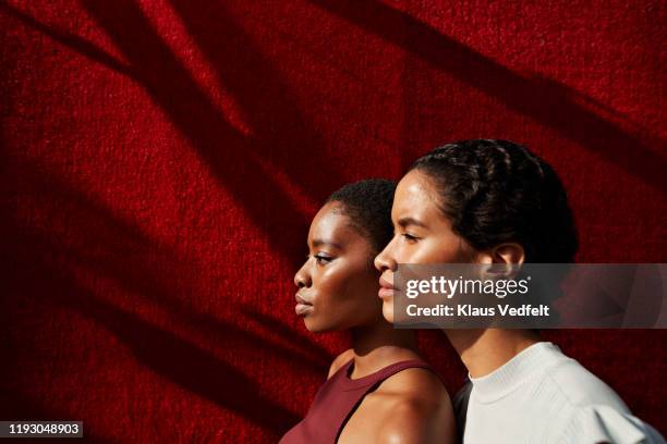 side view of women standing against red wall - red couple stock-fotos und bilder