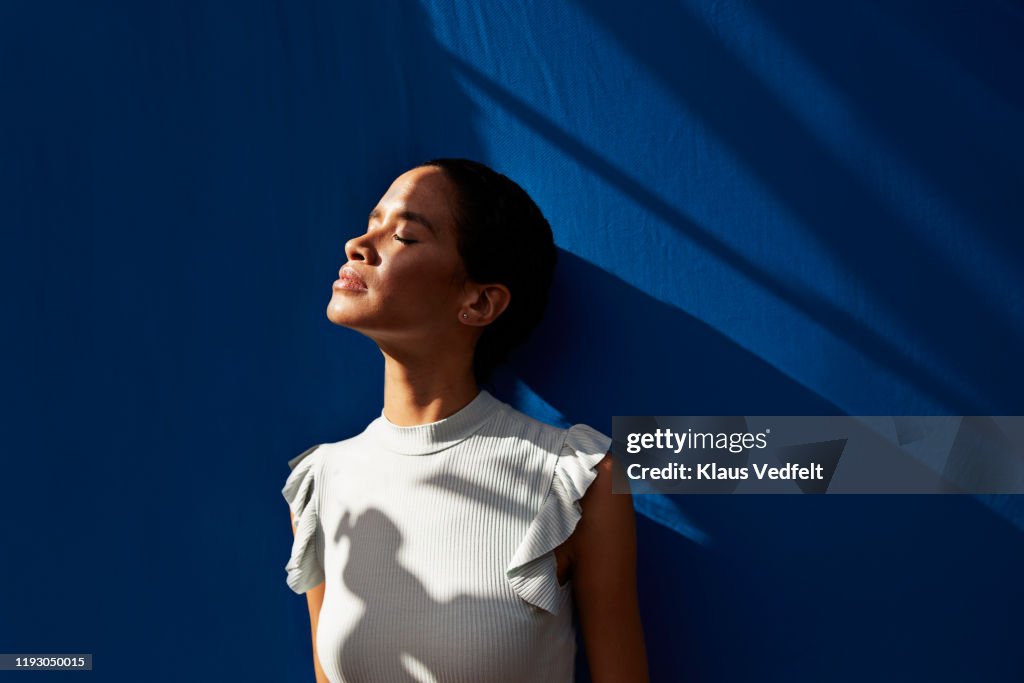 Thoughtful woman standing against blue wall