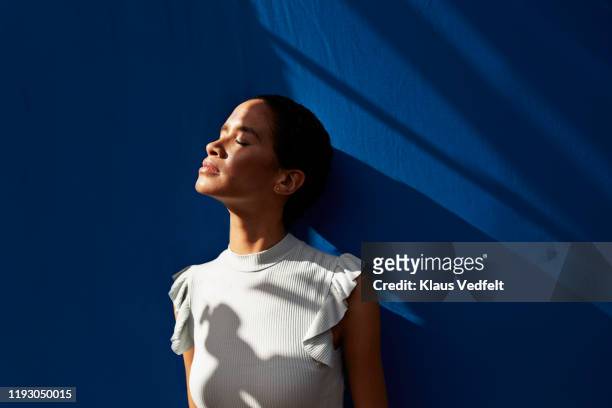 thoughtful woman standing against blue wall - serene people stock pictures, royalty-free photos & images