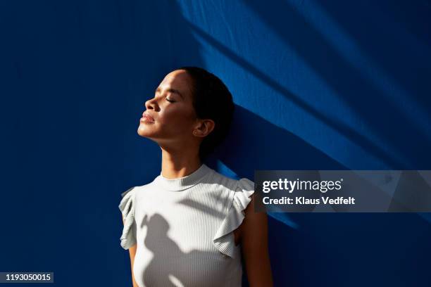 thoughtful woman standing against blue wall - simetria - fotografias e filmes do acervo