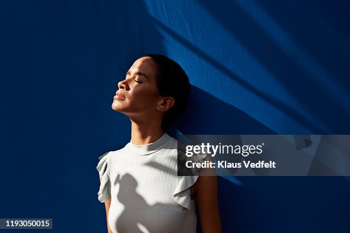 Thoughtful woman standing against blue wall Thoughtful woman standing against blue wall