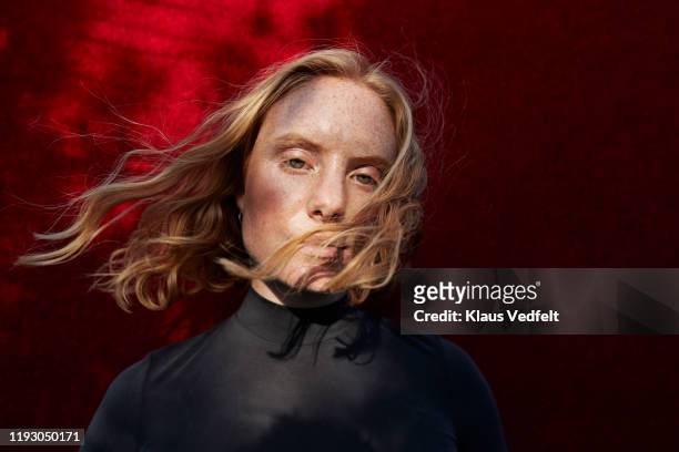 woman with tousled hair standing against red wall - tossing hair facing camera woman outdoors stock-fotos und bilder
