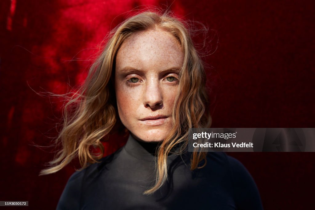 Close-up of serious woman standing against red wall