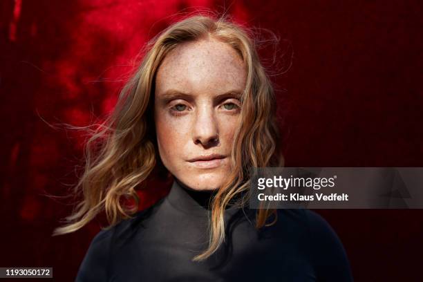 close-up of serious woman standing against red wall - emotional strength stock pictures, royalty-free photos & images