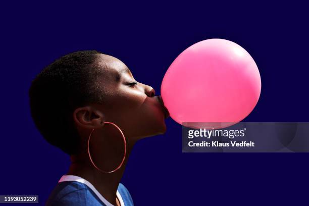 side view of young woman blowing balloon - ohrring stock-fotos und bilder