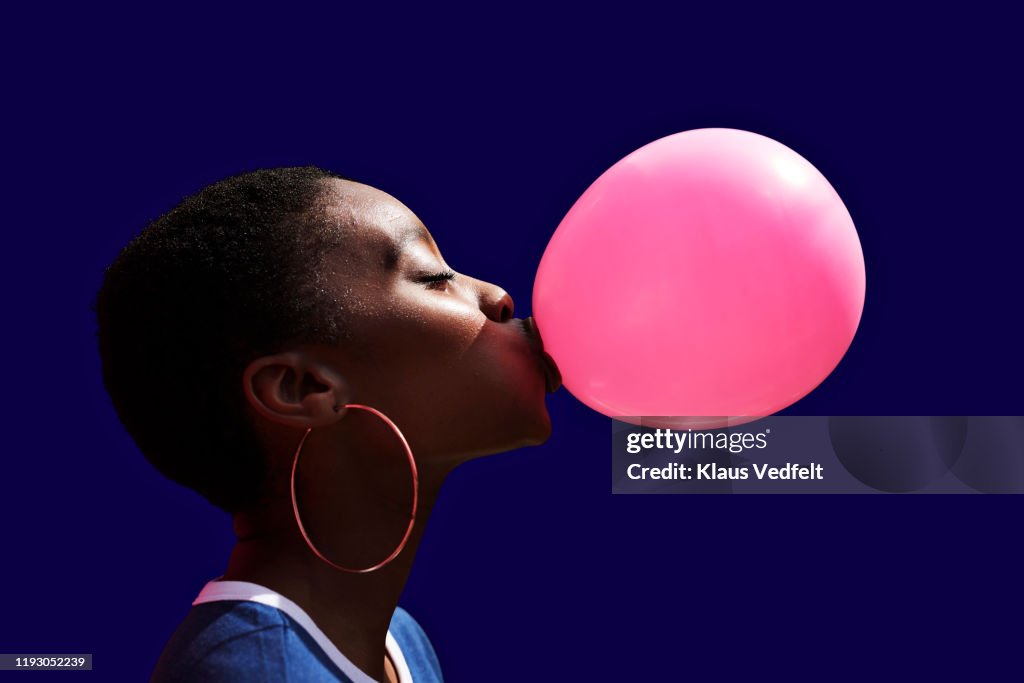 Side view of young woman blowing balloon