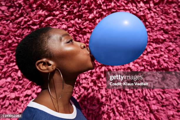 side view of woman blowing balloon against wall - black hair texture stock pictures, royalty-free photos & images