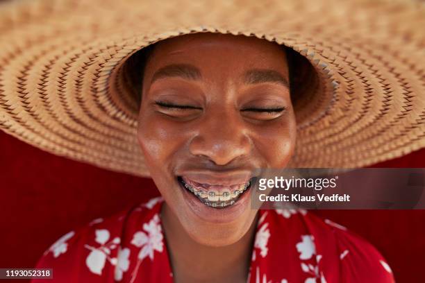 smiling woman wearing sun hat against red wall - adult retainer stock-fotos und bilder