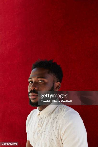 portrait of young man against red wall - polo shirt imagens e fotografias de stock